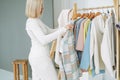 Young blonde woman stylist seller chooses clothes on hanger in bright studio Royalty Free Stock Photo