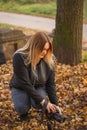 A young blonde woman  takes picture in an autumn park. Yellow, dry leaves on the ground.Fall time Royalty Free Stock Photo