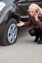 A young blonde woman talking on a mobile phone near her car with a flat tire