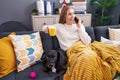 Young blonde woman talking on smartphone drinking coffee sitting on sofa with dog at home Royalty Free Stock Photo