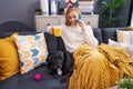 Young blonde woman talking on smartphone drinking coffee sitting on sofa with dog at home Royalty Free Stock Photo