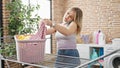 Young blonde woman talking on smartphone hanging clothes on clothesline at laundry room