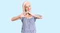 Young blonde woman with tattoo wearing casual clothes smiling in love showing heart symbol and shape with hands