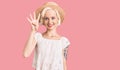 Young blonde woman with tattoo wearing summer hat showing and pointing up with fingers number four while smiling confident and Royalty Free Stock Photo