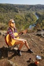 Young blonde woman tourists with guitar on cliff over river and Royalty Free Stock Photo