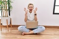 Young blonde woman using computer laptop sitting on the floor at the living room celebrating crazy and amazed for success with Royalty Free Stock Photo