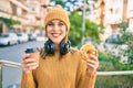 Young blonde woman using headphones and having breakfast at the city