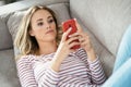 Young blonde woman using her smartphone lying on the sofa. Royalty Free Stock Photo