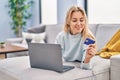 Young blonde woman using laptop and credit card lying on sofa at home Royalty Free Stock Photo