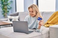 Young blonde woman using laptop and credit card lying on sofa at home Royalty Free Stock Photo