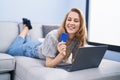 Young blonde woman using laptop and credit card lying on sofa at home Royalty Free Stock Photo