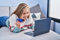 Young blonde woman using laptop and credit card lying on sofa at home Royalty Free Stock Photo