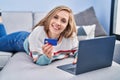 Young blonde woman using laptop and credit card lying on sofa at home Royalty Free Stock Photo
