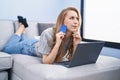 Young blonde woman using laptop and credit card lying on sofa at home Royalty Free Stock Photo