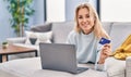 Young blonde woman using laptop and credit card lying on sofa at home Royalty Free Stock Photo