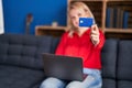 Young blonde woman using laptop and credit card sitting on sofa at home Royalty Free Stock Photo
