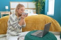 Young blonde woman using laptop drinking coffee at bedroom