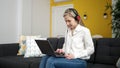 Young blonde woman using laptop and headphones sitting on sofa at home Royalty Free Stock Photo