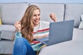 Young blonde woman using laptop at home screaming proud, celebrating victory and success very excited with raised arm Royalty Free Stock Photo