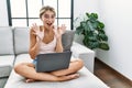 Young blonde woman using laptop at home sitting on the sofa celebrating crazy and amazed for success with arms raised and open Royalty Free Stock Photo