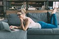 Young blonde woman using laptop while lying on sofa in living Royalty Free Stock Photo