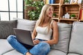 Young blonde woman using laptop sitting on sofa at home Royalty Free Stock Photo