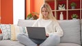 Young blonde woman using laptop sitting on sofa at home Royalty Free Stock Photo