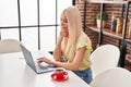 Young blonde woman using laptop sitting on table at home