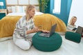 Young blonde woman using laptop and smartphone sitting on floor at bedroom Royalty Free Stock Photo