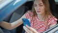 Young blonde woman using smartphone driving car at street Royalty Free Stock Photo