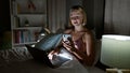 Young blonde woman using smartphone and laptop sitting on bed at bedroom Royalty Free Stock Photo