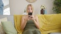 Young blonde woman using smartphone with serious face at home Royalty Free Stock Photo