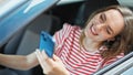 Young blonde woman using smartphone sitting on car at street Royalty Free Stock Photo