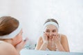 Young blonde woman washes face pure water in bathroom sink. Teen girl cleanse face skin. Self Care morning routine woman