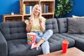 Young blonde woman watching movie sitting on sofa at home Royalty Free Stock Photo