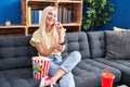 Young blonde woman watching movie sitting on sofa at home Royalty Free Stock Photo