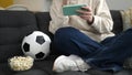 Young blonde woman watching soccer match on smartphone sitting on sofa at home Royalty Free Stock Photo