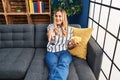 Young blonde woman watching tv eating chips potatoes sitting on sofa at home Royalty Free Stock Photo