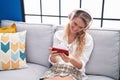 Young blonde woman watching video on smartphone sitting on sofa at home Royalty Free Stock Photo