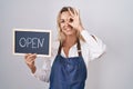 Young blonde woman wearing apron holding blackboard with open word smiling happy doing ok sign with hand on eye looking through Royalty Free Stock Photo