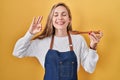 Young blonde woman wearing apron tasting food holding wooden spoon smiling with a happy and cool smile on face Royalty Free Stock Photo