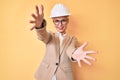 Young blonde woman wearing architect hardhat looking at the camera smiling with open arms for hug Royalty Free Stock Photo