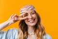 Young blonde woman wearing bandanna smiling and gesturing peace sign