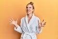 Young blonde woman wearing bathrobe crazy and mad shouting and yelling with aggressive expression and arms raised Royalty Free Stock Photo