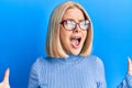 Young blonde woman wearing casual clothes and glasses crazy and mad shouting and yelling with aggressive expression and arms Royalty Free Stock Photo