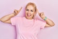 Young blonde woman wearing casual pink t shirt smiling amazed and surprised and pointing up with fingers and raised arms Royalty Free Stock Photo