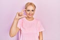 Young blonde woman wearing casual pink t shirt smiling and confident gesturing with hand doing small size sign with fingers Royalty Free Stock Photo