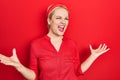 Young blonde woman wearing casual red shirt crazy and mad shouting and yelling with aggressive expression and arms raised Royalty Free Stock Photo