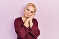Young blonde woman wearing casual winter sweater sleeping tired dreaming and posing with hands together while smiling with closed Royalty Free Stock Photo
