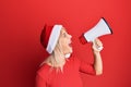 Young blonde woman wearing christmas hat screaming using megaphone over isolated red background Royalty Free Stock Photo